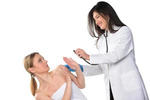 Caring young female doctor in medical facemask hold stethoscope listen to patient heart in hospital. photo