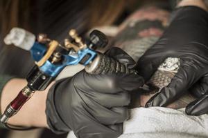 máquina de tatuaje de cerca. mujer creando una imagen a mano con ella en el salón foto