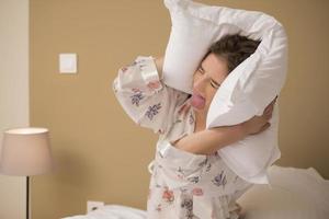 Young woman hugging pillow on comfortable bed with silky linens photo