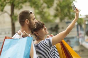 Portrait of cheerful Caucasian young couple man and woman holding many paper bags after shopping while walking and talking on street. Happy family couple with packages outdoor. Buying concept photo