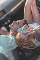 Friends having fun at car trip around the world. Couple in love with arms up on a convertible car. photo