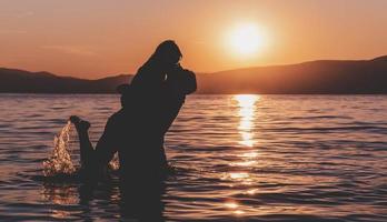 silhouettes in love romantic couple lovers hugging, kissing, touching, eye contact at sunset, sunrise on the background of the sea, the sun, the clouds in fiery red, orange colors photo