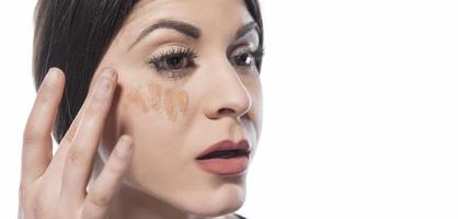 Portrait of a young woman applying liquid make up on her face. Isolated on white background photo