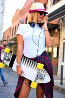 hermosa chica hipster con patineta con gafas de sol en la ciudad. foto