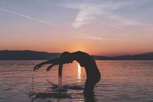 silhouettes of beautiful female model at sunset, sunrise on the background of the sea, the sun, the clouds in fiery red, orange colors photo