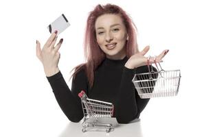 Happy female holding credit cards and a small empty shopping cart isolated on white background photo