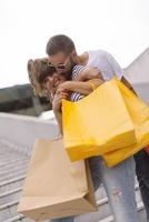 Portrait of cheerful Caucasian young couple man and woman holding many paper bags after shopping while walking and talking on street. Happy family couple with packages outdoor. Buying concept photo