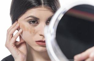Portrait of a young woman applying liquid make up on her face. Isolated on white background photo