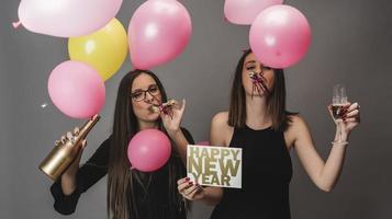 Two female friends celebrating New Year with confetti and champagne holding sign. isolated photo