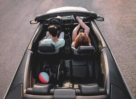Friends having fun at car trip around the world. Couple in love with arms up on a convertible car. photo