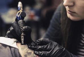 máquina de tatuaje de cerca. mujer creando una imagen a mano con ella en el salón foto