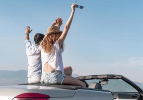 Friends having fun at car trip around the world. Couple in love with arms up on a convertible car. photo