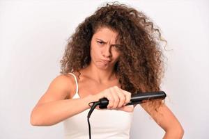 nice-looking attractive mad irritated wavy-haired girl ironing straightening messy curls keratin therapy treatment photo