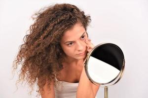 mujer mirándose en el espejo, compruebe la cara después de la mascarilla, el tratamiento de belleza con crema, se siente satisfecha foto