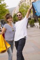 Portrait of cheerful Caucasian young couple man and woman holding many paper bags after shopping while walking and talking on street. Happy family couple with packages outdoor. Buying concept photo