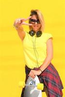 Portrait of happy beautiful blonde girl  hold her wooden longboard skateboard on yellow background wall, look to the camera and smile. Urban scene, city life. Hipster cute lady. photo