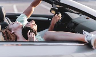 Friends having fun at car trip around the world. Couple in love with arms up on a convertible car. photo