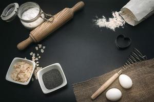 Bakery background. Baking ingredients and kitchen utensils on the black background. Flour, almond nuts, eggs. Top view, copy space. Modern cooking composition. Free space for text. photo