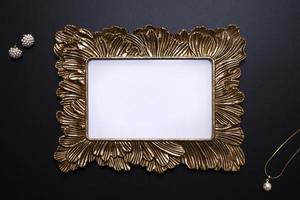 Elegant background, template for text, logo or picture. Golden decorative picture frame and jewellery on the black background. Free space, copy space. photo