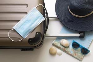 Travel during the time of COVID-19. Medical mask, suitcase, sun glasses, map, seashells on the white background. Vacation, holidays in corona times. photo