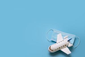 Travel during the time of COVID-19. Medical mask and mini airplane on the blue background. Free space for text. Vacation, holidays, flight in corona times. photo
