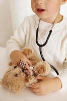 Cute little boy playing doctor at home and curing plush toy. Sweet toddler child using stethoscope. Having fun. Kids and medicine, healthcare.