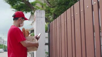 delivery man confirms checks the address through the application system.One woman ordered food online to eat at home. delivery man put a mask sent food online parcels from on the door. video