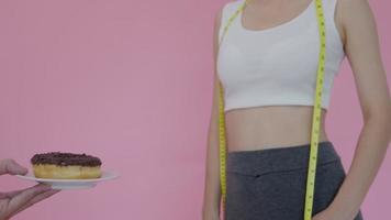 dieta y dieta. belleza cuerpo femenino delgado confundir donut. mujer con ropa de ejercicio logra el objetivo de pérdida de peso para una vida saludable, loca por la delgadez, cintura delgada, nutricionista. video