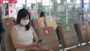 nuevo concepto normal. las mujeres asiáticas usan una máscara y se sientan entre sillas para reducir la propagación del coronavirus. los turistas esperan para subirse a los aviones durante el brote de covid-19. video