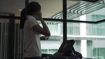 hermosa mujer asiática se está poniendo auriculares y tocando música en su teléfono. escuchar música mientras se hace ejercicio es una forma de relajarse durante las actividades. aptitud para el concepto de salud. video