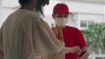deliveryman in looks nice wearing sanitary masks. food order online and Fast delivery. Deliver man check location customer by mobile phone. Woman write down for confirm receive food. video