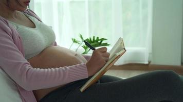 concepto de preparación para la madre. una mujer embarazada escribe en un libro sobre equipos para recién nacidos. la cesárea es una manera para que las mujeres embarazadas sepan una fecha de parto. video