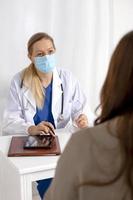 Young brunette woman having consultation at doctor office during coronavirus and flu outbreak. Female doctor wearing facemask. Virus protection. Covid 19. photo