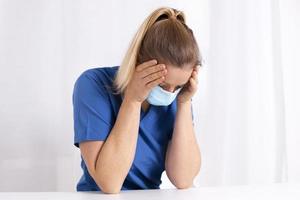 Tired and exhausted nurse or doctor. Stressed female medical worker with protective face mask, depressed after working over hours due to coronavirus outbreak. Covid 19. Medicine, healthcare, pandemic photo