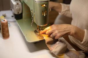 Closeup view of womans hands sewing fabric with a vintage, retro sewing machine. Fashion, creation and tailoring. Process of sewing in atelier or workshop. photo