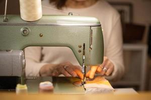 Closeup view of womans hands sewing fabric with a vintage, retro sewing machine. Fashion, creation and tailoring. Process of sewing in atelier or workshop. photo