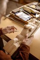 Artist is grinding wooden sculpture. Carpenter working with wood in workshop. Man and his hobby. Closeup view, only hands in frame. photo