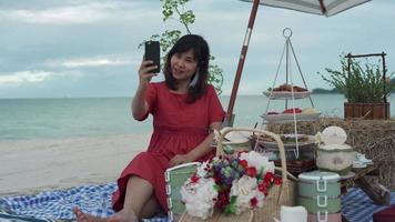 Beautiful Asian woman taking pictures of herself while traveling at sea. A woman is having a VDO conference with her family about food attractions by the sea. concept of relaxation video