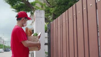 repartidor asiático con máscaras sanitarias y guantes durante el parto. pedido de comida en línea y entrega rápida. entregar al hombre verificar la ubicación por teléfono móvil. video