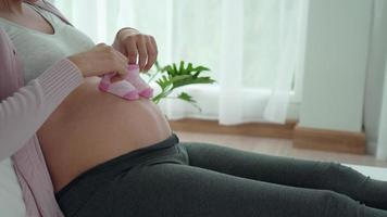 la mujer embarazada está jugando con su bebé en sus zapatos para caminar en el vientre. la mujer está haciendo actividades para relajar su embarazo. actividad conceptual para mujeres embarazadas y relajación para reducir la depresión. video