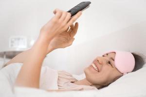 Relaxed young woman using a smartphone in the morning on the bed at home. Happy and smiling girl using a mobile phone. Woman texting, checking social apps, makes video call or playing with smartphone. photo
