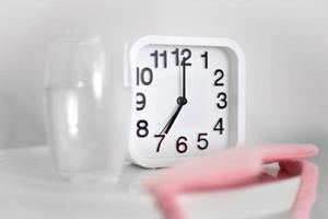 White alarm clock and glass of water on table in bedroom. Wake up early in the morning by the alarm bell and drink water. photo
