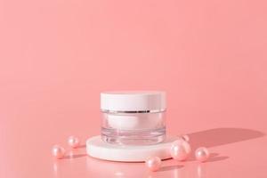 White unbranded cosmetic cream jar standing on white podium. Skin care product presentation on the pink background with pearls. Trendy mockup. Skincare, beauty and spa. photo