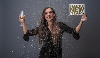 hermosa mujer celebrando el año nuevo con confeti y champán con cartel. aislado foto