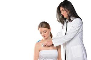 Caring young female doctor in medical facemask hold stethoscope listen to patient heart in hospital. photo