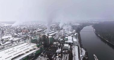 vol près des tuyaux avec de la fumée blanche de la scierie de l'usine de menuiserie près de la rivière. concept de pollution de l'air sur le paysage industriel en hiver avec de la neige video