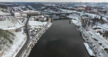 flight and aerial view on winter city with bridge across a wide river with snow