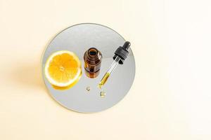 moisturizing serum with peptides based on lemon essential oil to increase skin elasticity, with vitamin C stands on a round cosmetic mirror. top view. photo
