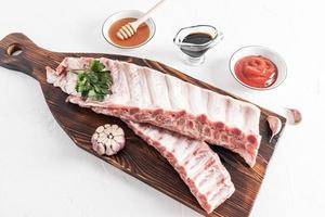 raw pig meat ribs on a cutting board with various bowls of marinade sauces. the concept of cooking meat. photo