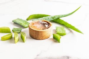 Universal aloe vera gel in a wooden bowl on a white marble background among the juicy leaves of the plant. care for the skin of the face and body. photo